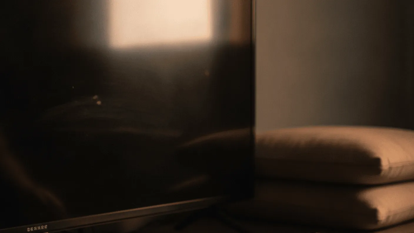 A black streaming box sits on a wooden shelf beneath a television, a hand reaches for its remote.
